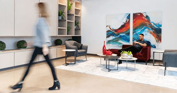 A woman in a blue shirt and black pants walks through a living room.